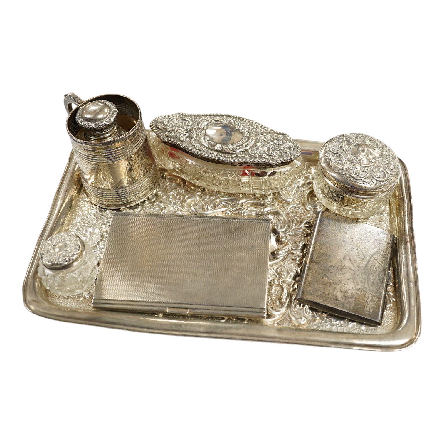 A George V repousse silver dressing table tray, William Neale Ltd, Birmingham, 1910, 29.1cm, two silver cigarette cases, a George III silver christening mug (a.f.) and four silver mounted glass toilet jars. Condition - p